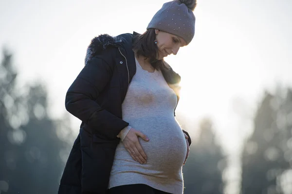 从下面看去 一个怀孕的年轻女子站在外面 慈祥地望着自己肿胀的腹部 轻轻碰着它 — 图库照片