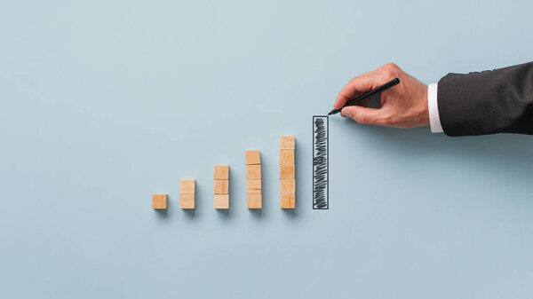 Hand of a businessman drawing financial graph bar in a conceptual image of economy and stock market. Over light blue background.