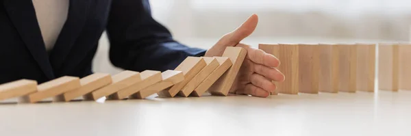 Wide view image of hand of businesswoman interrupting collapsing dominos in a conceptual image of preventing financial and market depression.