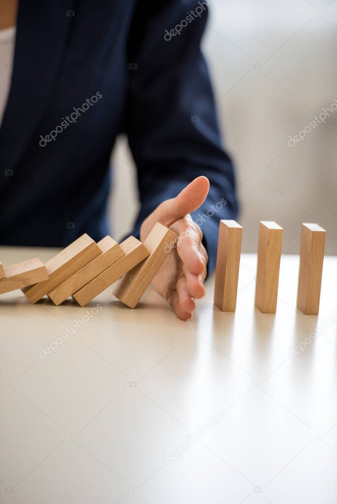 Closeup view of businesswoman interrupting collapsing dominos with her hand in conceptual image of business depression prevention.