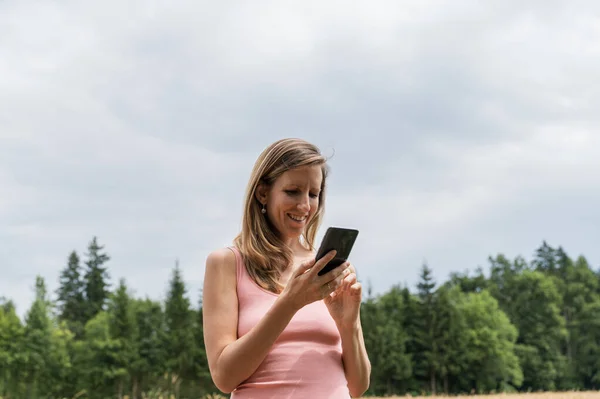 Uśmiechnięta Młoda Kobieta Zewnątrz Naturze Patrząc Telefon Komórkowy — Zdjęcie stockowe