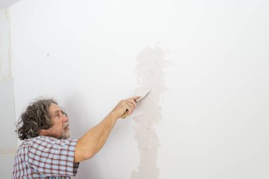 Kurulum hatlarının deliğini kapamak için duvarı spatulayla kaplayan işçiler.