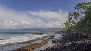 Okyanusun mavi dalgalarının vurduğu taşlı bir sahil. Gökyüzünde güzel bulutlar var..