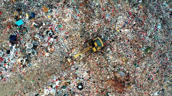 Tractor on a mountain of garbage. Tractor with a bucket on the garbage. Photo taken from above. Below the tents of the homeless. Save the planet.