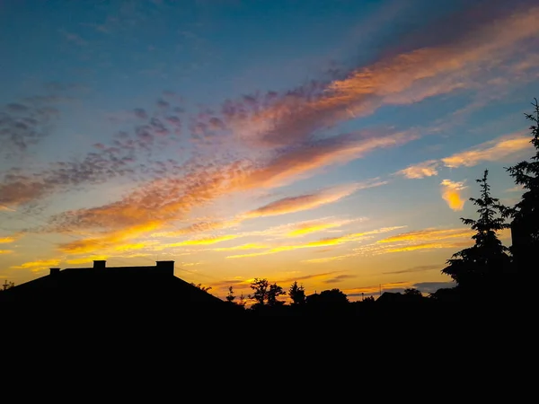 建物や木々のシルエットの上に曇ったカラフルな夕日 — ストック写真