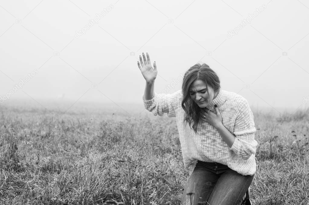 Girl closed her eyes on the knees, praying in a field during beautiful fog. 