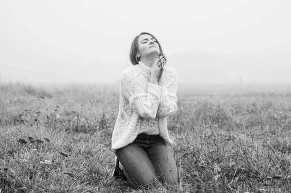 A lány térdre hunyta a szemét, és imádkozott a mezőn a gyönyörű köd alatt.. — Stock Fotó