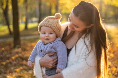Sonbahar yürüyüşünde mutlu bir aile. Anne küçük oğlunu kollarında tutuyor ve güzel sonbahar doğasının tadını çıkarıyor.. 