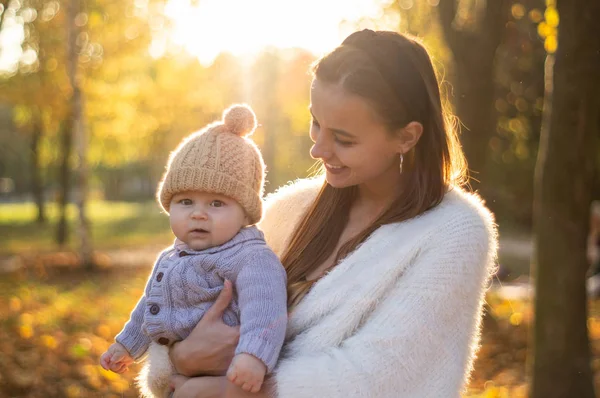 Famiglia felice in passeggiata autunnale. Madre tiene in braccio il piccolo figlio e gode della bella natura autunnale in un parco . — Foto Stock