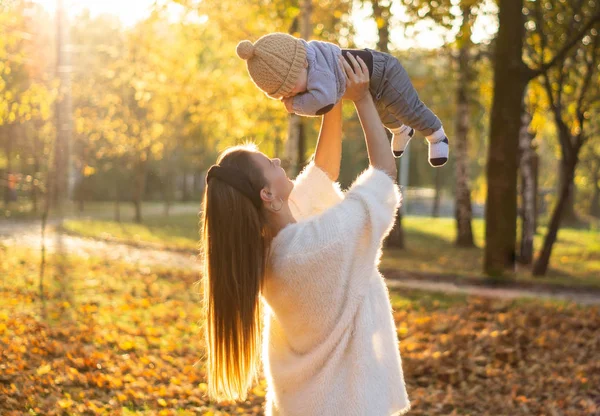 Šťastná rodina na podzimní procházce. Matka drží malého syna v náručí a užívá si krásné podzimní přírody v parku. — Stock fotografie