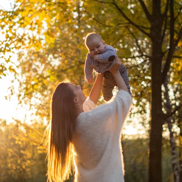 Famiglia felice in passeggiata autunnale. Madre tiene in braccio il piccolo figlio e gode della bella natura autunnale in un parco . — Foto Stock