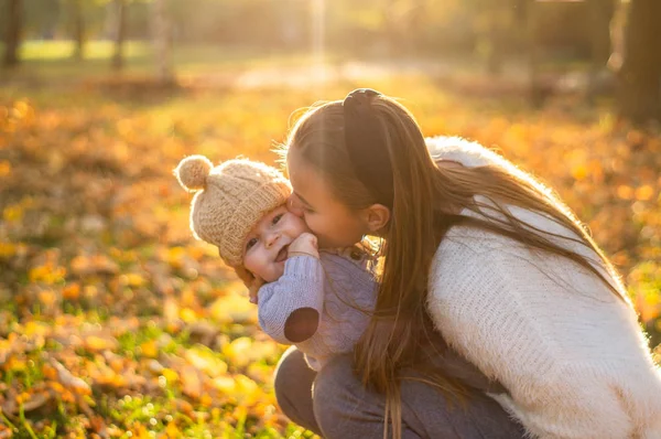 Gelukkige familie op herfstwandeling. Moeder houdt zoontje in haar armen en geniet van de prachtige herfstnatuur in een park. — Stockfoto