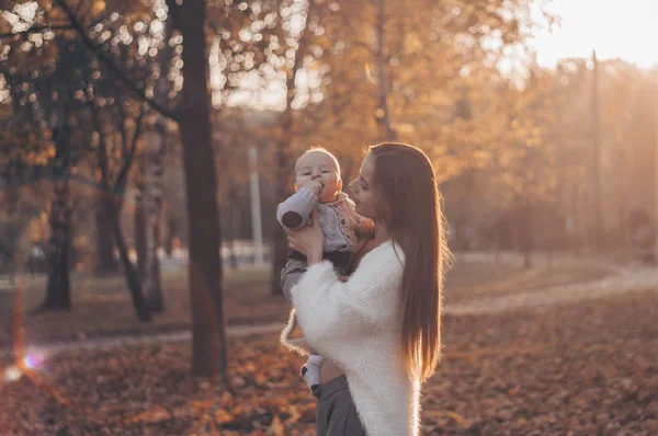 Šťastná rodina na podzimní procházce. Matka drží malého syna v náručí a užívá si krásné podzimní přírody v parku. — Stock fotografie