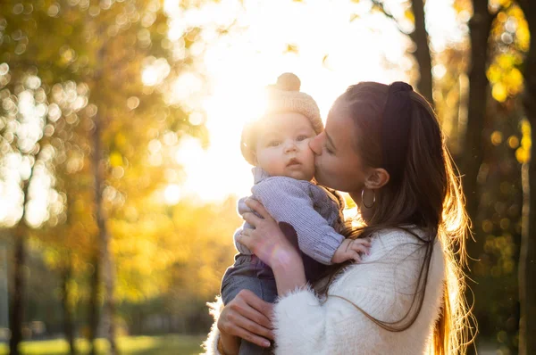 Famiglia felice in passeggiata autunnale. Madre tiene in braccio il piccolo figlio e gode della bella natura autunnale in un parco . — Foto Stock