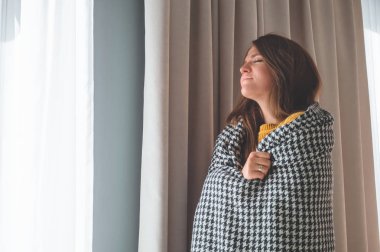 Pencerede sıcak ekoseli bir kadın duruyor. Sonbahar-kış zamanı.