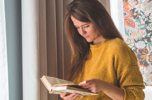 Wanita muda yang menarik membaca buku di rumah. Gadis bijaksana membaca buku penting — Stok Foto