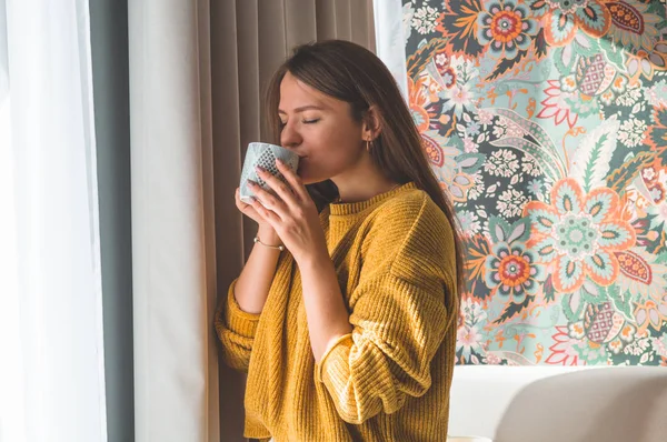 Mujer con una taza de bebida caliente junto a la ventana. Mirando a la ventana y beber té . — Foto de Stock