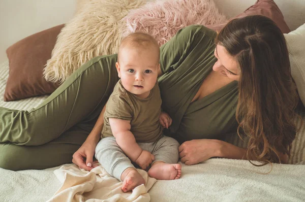 Házi portré egy kisfiúról anyával az ágyon. Anya öleli és csókolja a gyermekét. — Stock Fotó