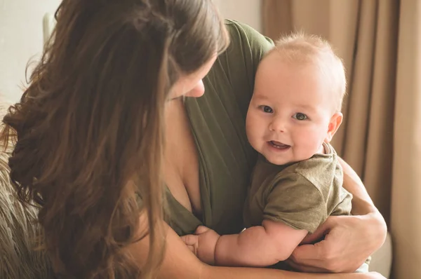 Retrato casero de un niño con madre en la cama. Mamá sosteniendo y besando a su hijo . — Foto de Stock