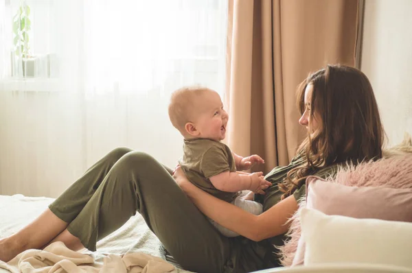 Retrato caseiro de um menino com a mãe na cama. Mãe segurando e beijando seu filho . — Fotografia de Stock