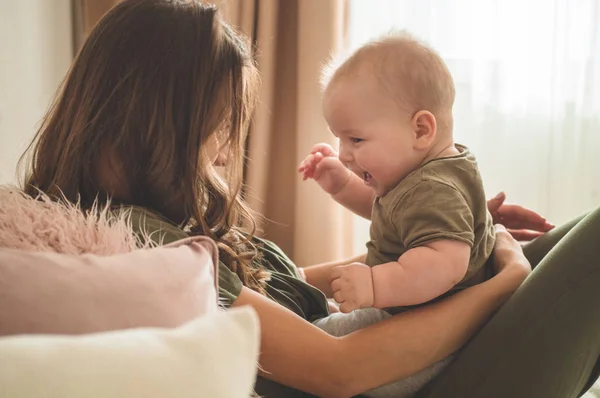 Házi portré egy kisfiúról anyával az ágyon. Anya öleli és csókolja a gyermekét. — Stock Fotó