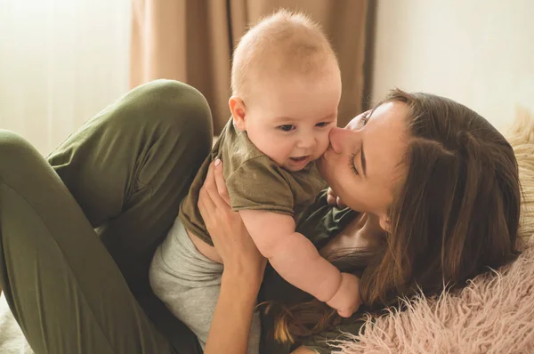 Portret chłopca z matką na łóżku. Mama trzyma i całuje swoje dziecko. — Zdjęcie stockowe