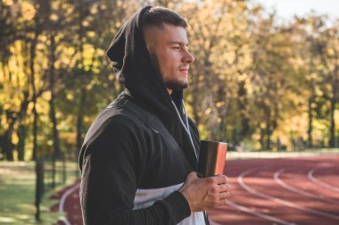 Stadyumda kaslı ve zayıf vücutlu bir erkek model sıcak çay içiyor.. 