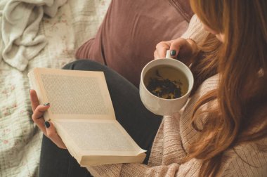 Sıcak çay içip kitap okuyan bir kadın. Geliştir ve rahatla