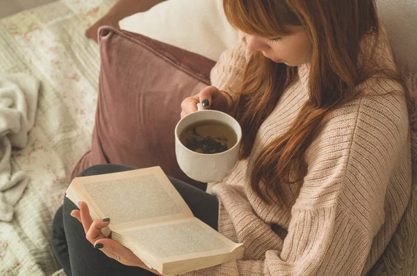 Mujer bebiendo té caliente y leyendo libro. Desarrollo y relajación — Foto de Stock