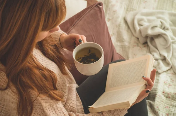 Mujer bebiendo té caliente y leyendo libro. Desarrollo y relajación — Foto de Stock