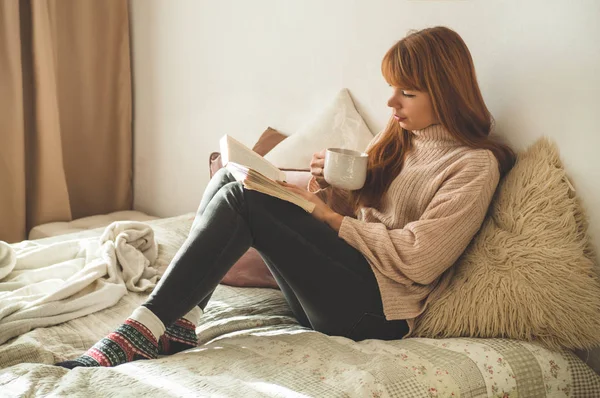 Mujer bebiendo té caliente y leyendo libro. Desarrollo y relajación — Foto de Stock