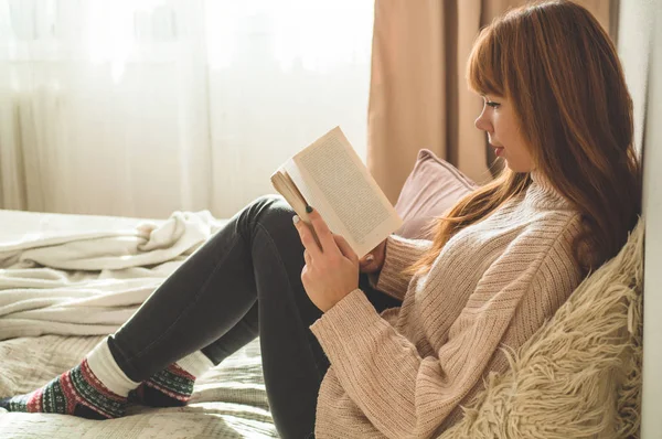 Una joven atractiva está leyendo un libro en casa. Chica reflexiva leyendo libro importante . — Foto de Stock