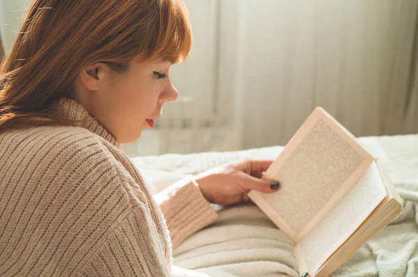 Uma jovem atraente está lendo um livro em casa. Menina pensativa lendo livro importante . — Fotografia de Stock