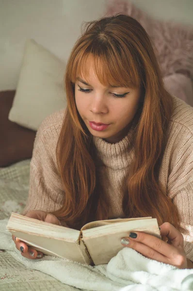 Uma jovem atraente está lendo um livro em casa. Menina pensativa lendo livro importante . — Fotografia de Stock