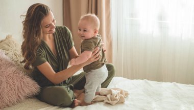 Yatakta annesi olan bir çocuğun ev portresi. Anne çocuğunu kucağına alıp öpüyor. İlk Adımlar.
