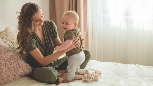 Portret chłopca z matką na łóżku. Mama trzyma i całuje swoje dziecko. Pierwsze kroki. — Zdjęcie stockowe