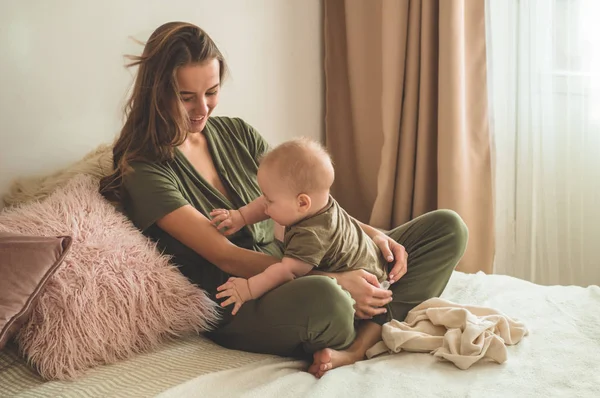 Retrato caseiro de um menino com a mãe na cama. Mãe segurando e beijando seu filho. Primeiros passos . — Fotografia de Stock