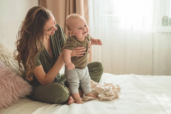 Portret chłopca z matką na łóżku. Mama trzyma i całuje swoje dziecko. Pierwsze kroki. — Zdjęcie stockowe