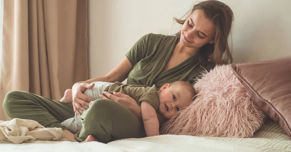 Házi portré egy kisfiúról anyával az ágyon. Anya öleli és csókolgatja a gyerekét. Első lépések. — Stock Fotó