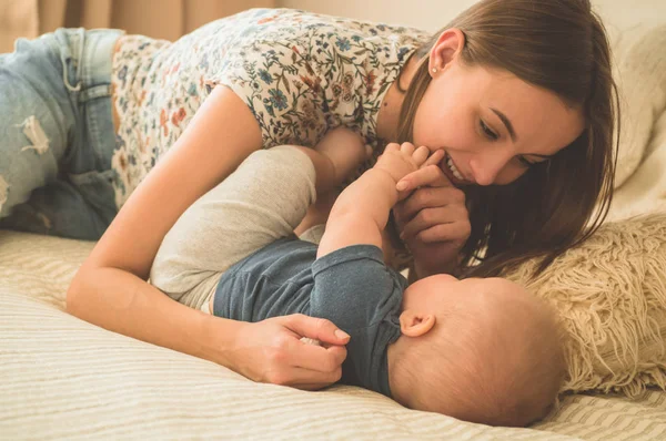 Miłość i rodzina. Portret chłopca z matką na łóżku. Mama grać i całować swoje dziecko — Zdjęcie stockowe