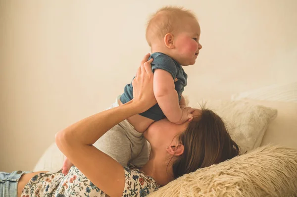 Szeretet és család. Házi portré egy kisfiúról anyával az ágyon. Anya játszik és megcsókolja a gyerekét. — Stock Fotó