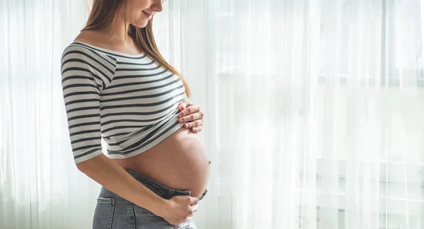 Feliz mujer embarazada con el vientre grande junto a la ventana. Conceptos de embarazo y familia — Foto de Stock