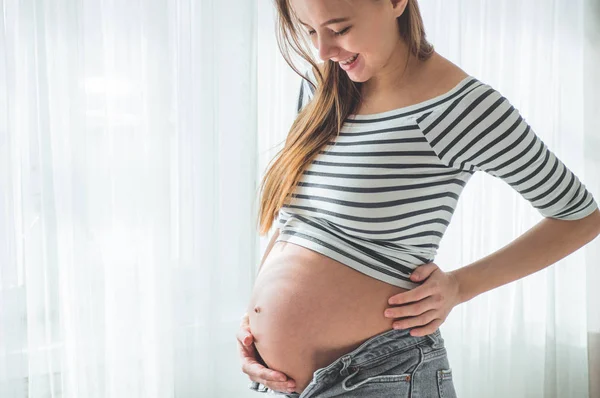 Ευτυχισμένη έγκυος γυναίκα με μεγάλη κοιλιά στο παράθυρο. Έννοιες της εγκυμοσύνης και της οικογένειας — Φωτογραφία Αρχείου