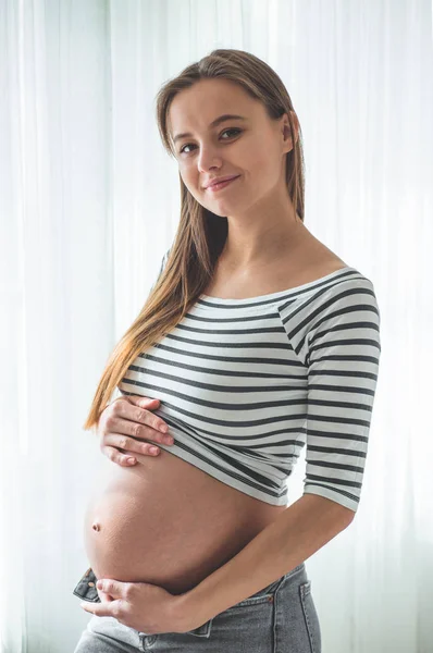 Heureuse femme enceinte avec un gros ventre près de la fenêtre. Concepts de grossesse et de famille — Photo