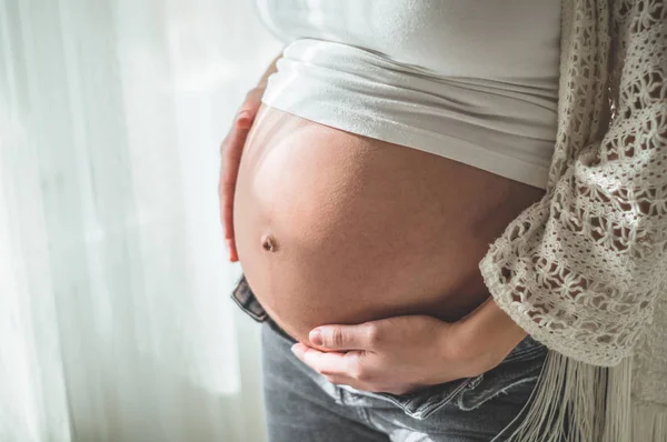 Heureuse femme enceinte avec un gros ventre près de la fenêtre. Concepts de grossesse et de famille — Photo