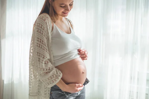 Szczęśliwa ciężarna kobieta z dużym brzuchem przy oknie. Pojęcia ciąża i rodzina — Zdjęcie stockowe