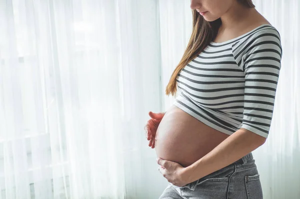 Heureuse femme enceinte avec un gros ventre près de la fenêtre. Concepts de grossesse et de famille — Photo