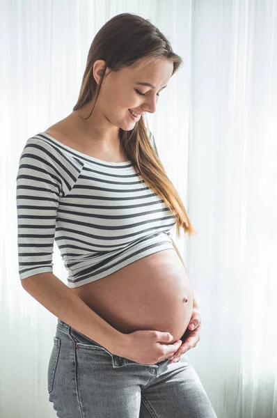 Feliz mujer embarazada con el vientre grande junto a la ventana. Conceptos de embarazo y familia — Foto de Stock