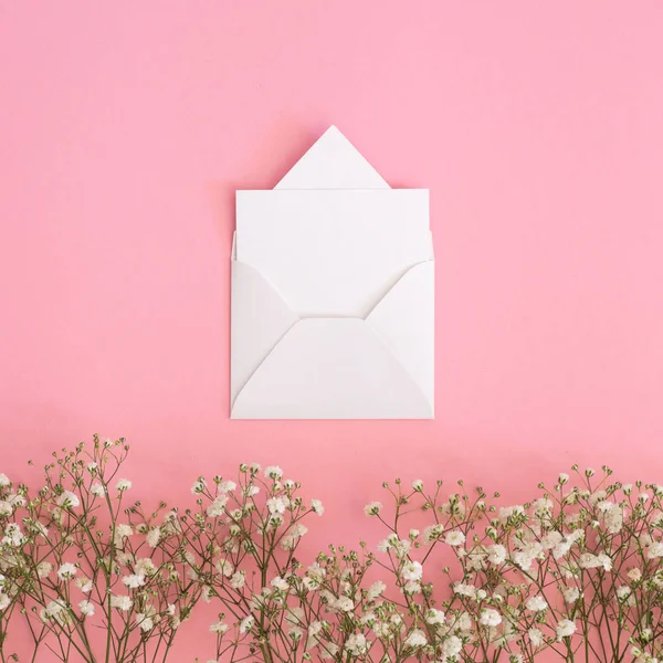 Cartão de saudação em branco, envelope kraft e flores de gypsophila em um fundo rosa — Fotografia de Stock