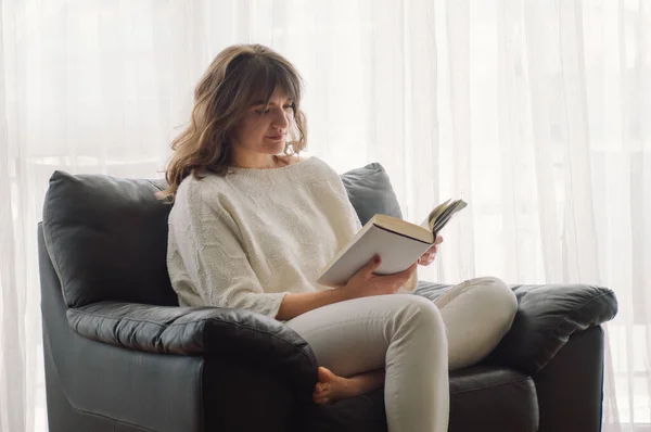 Wanita muda yang cantik membaca buku di rumah. Gadis bijaksana membaca buku penting — Stok Foto